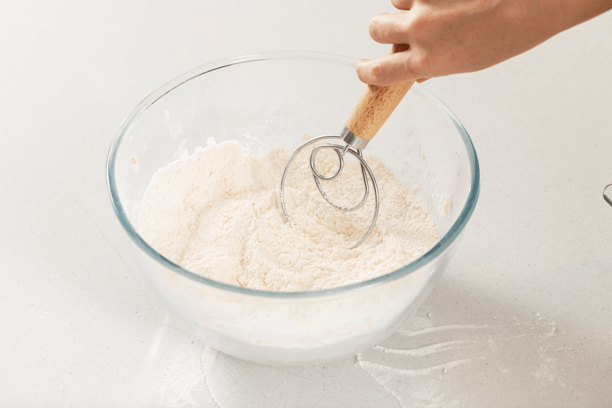 Person Using Danish Dough Whisk in Glass Bowl of Flour