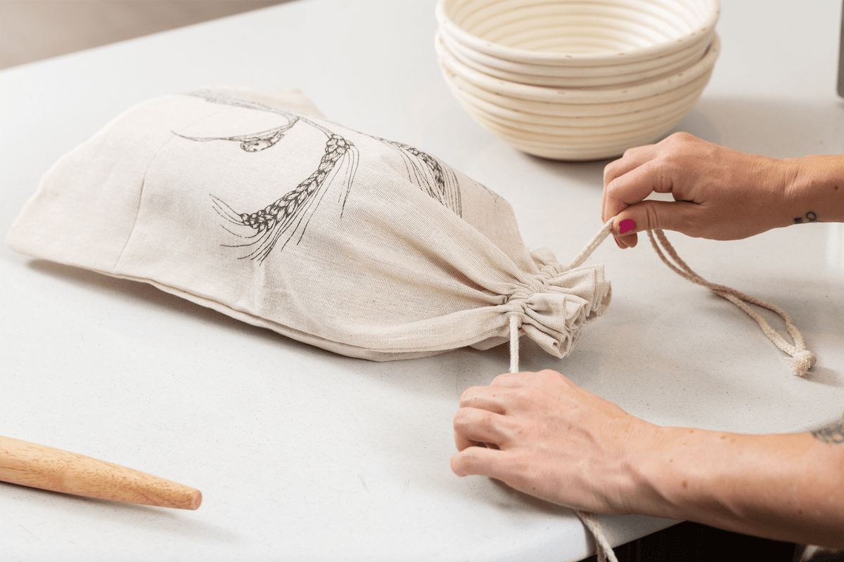 Person Tying Linen Bread Bag Closed with Bannetons in Background